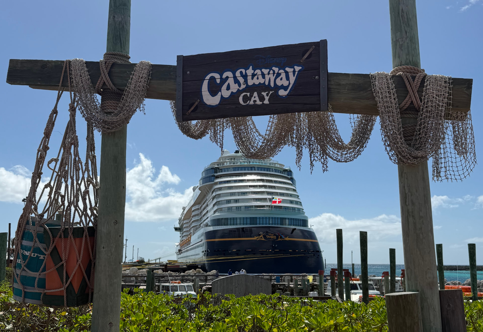 Disney cruise ship docked at Castaway Cay beneath a wooden welcome sign