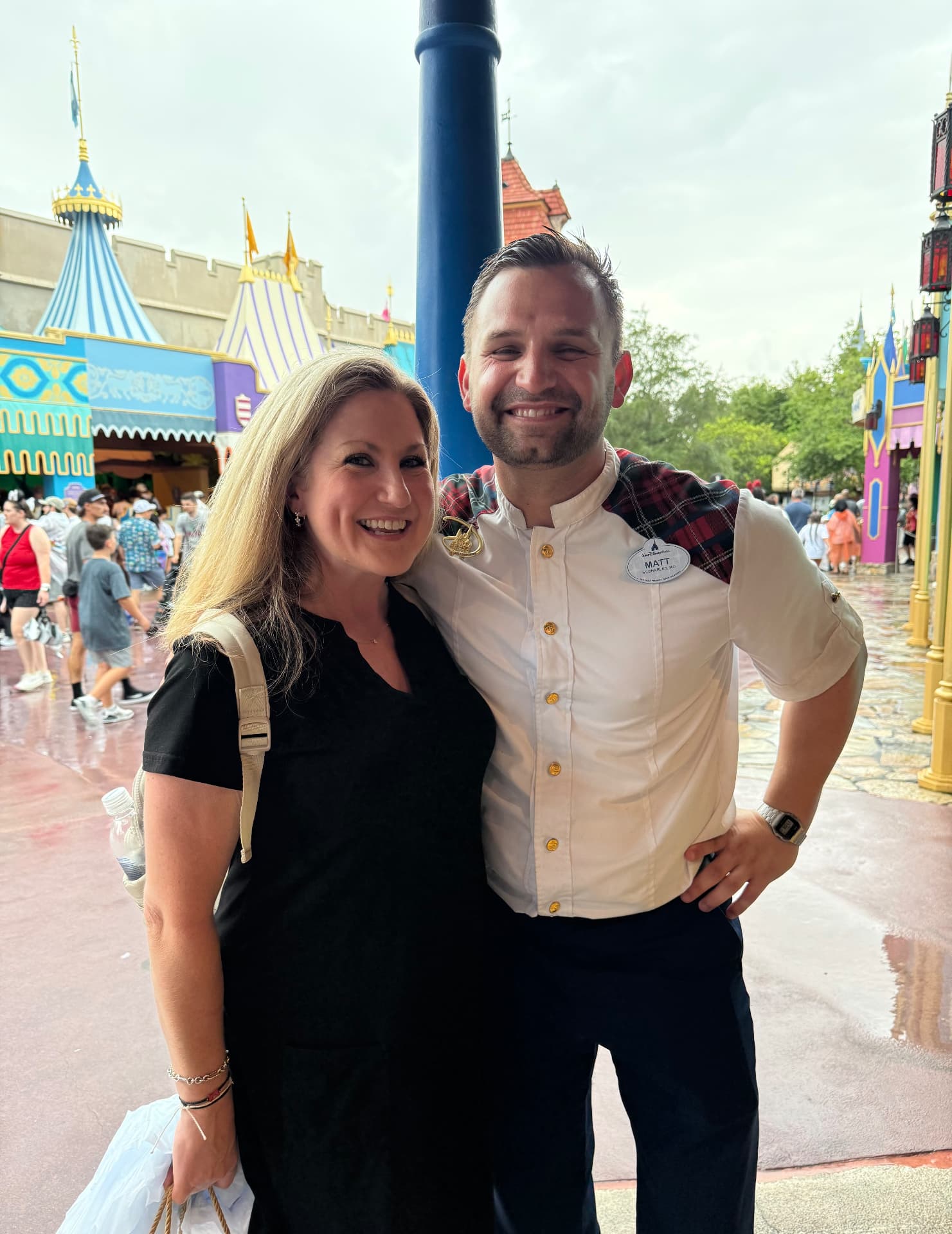 Bridget Edwards standing beside Matt, her Disney VIP Tour guide, in front of the storybook buildings of Fantasyland