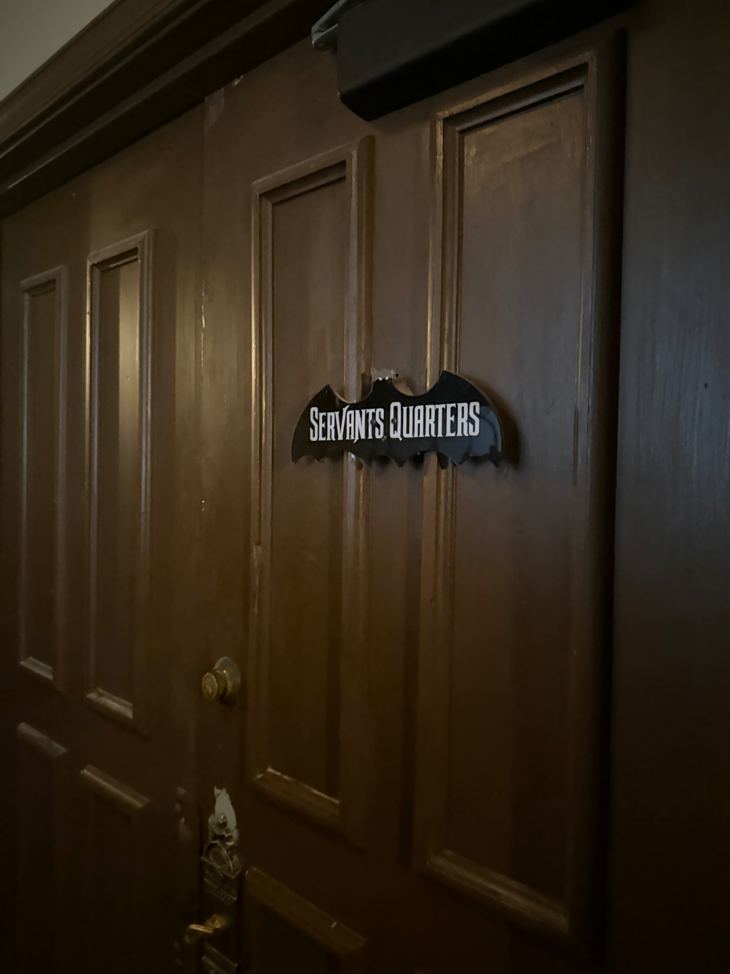 A dark wooden door with a bat-shaped sign reading Servants Quarters