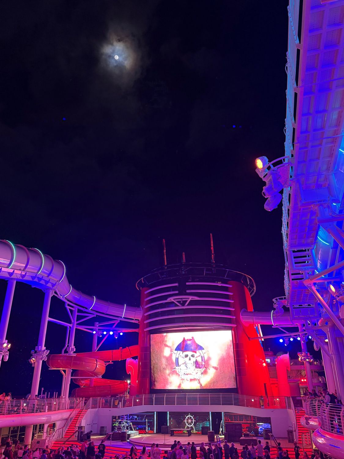 Guests gathered on deck at night for Pirate Night, with a stage and screens set into the ship's red funnel and the AquaDuck slide lit above