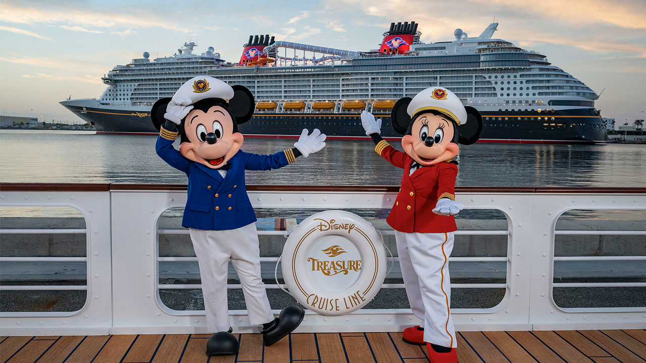 Mickey and Minnie Mouse in their captain's uniforms on deck with the Disney Treasure behind them