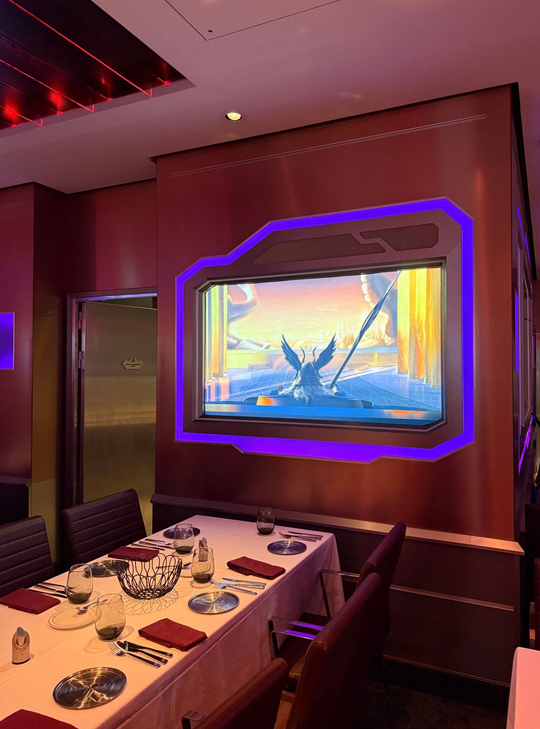 A set dining table beside a wall of glowing screens inside Worlds of Marvel on the Disney Destiny