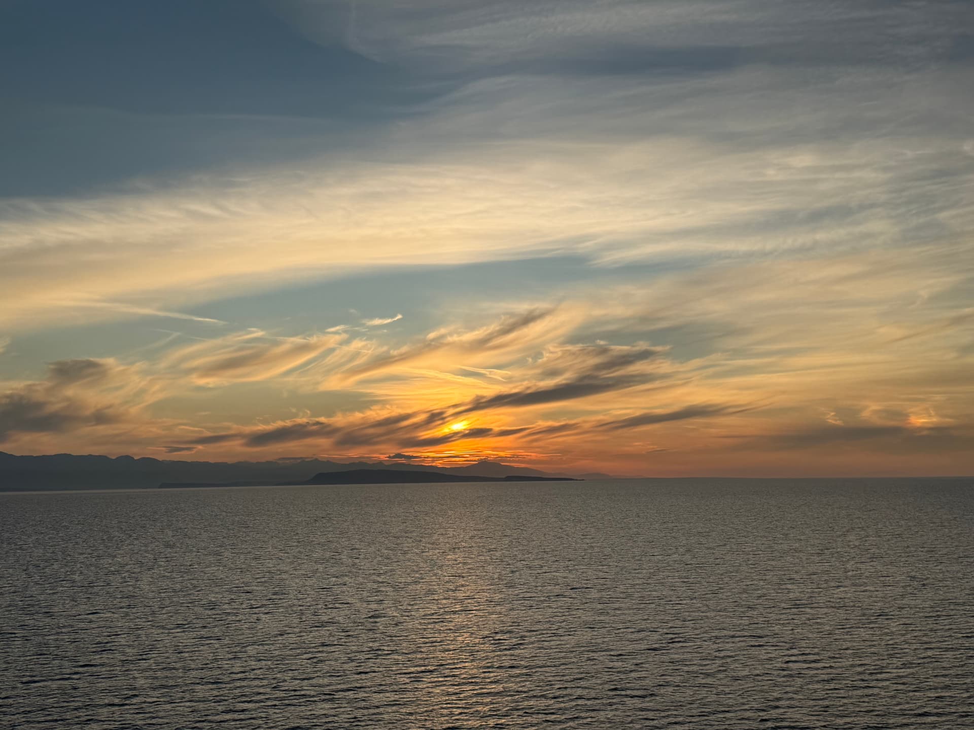A golden sunset over calm water with distant mountains, seen from a Celebrity cruise