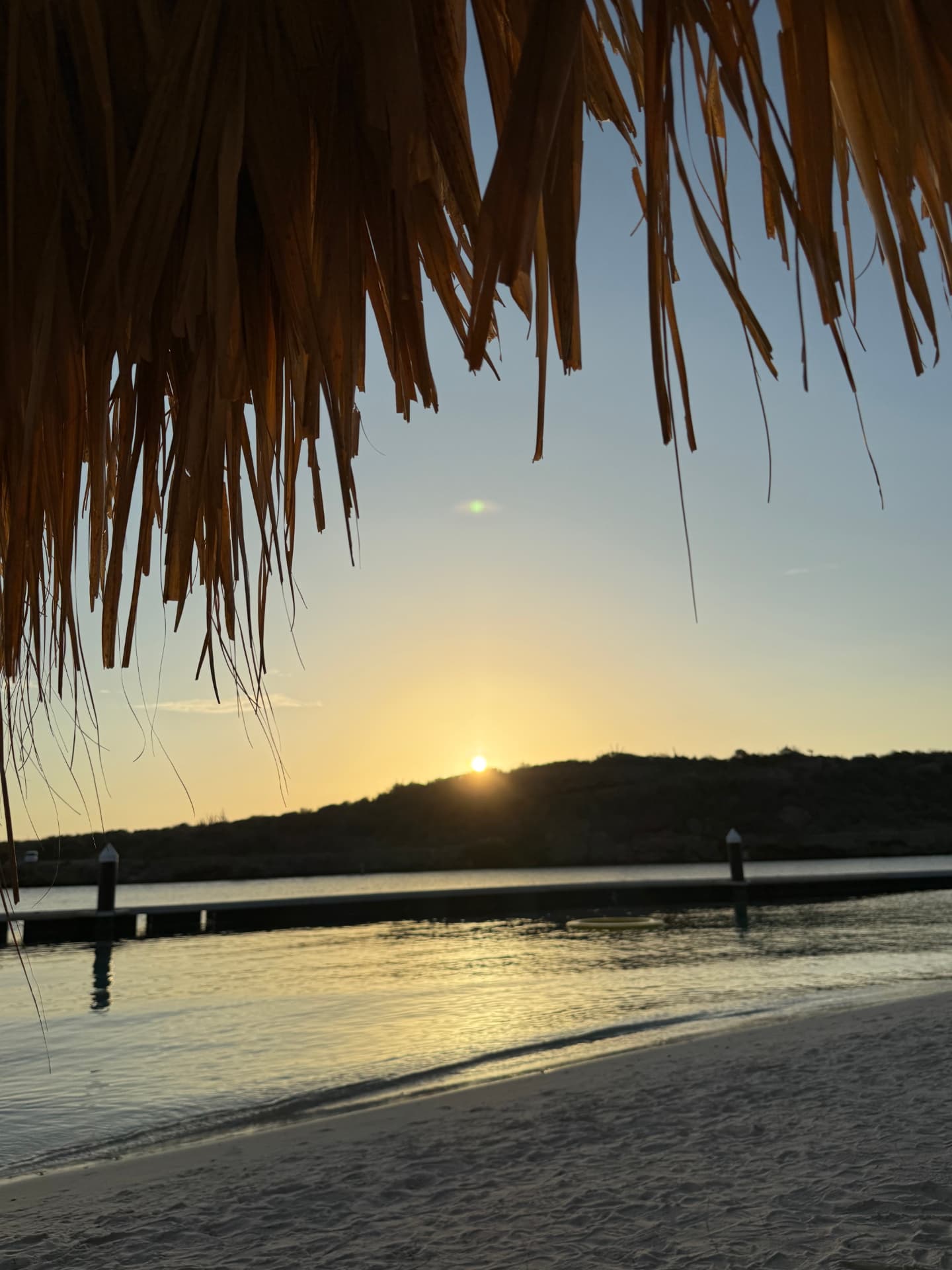 Golden sunset over a calm Caribbean cove beneath a thatched palapa