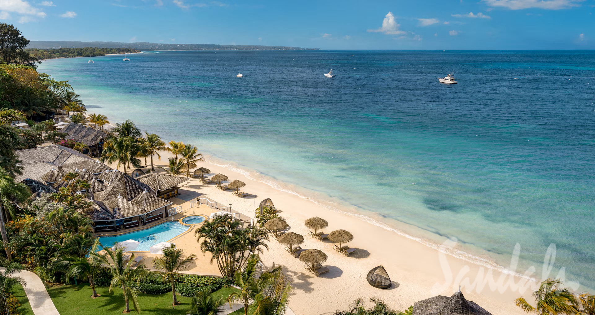 Aerial view of the white-sand beach, turquoise water, and thatched palapas at Sandals Jamaica Negril