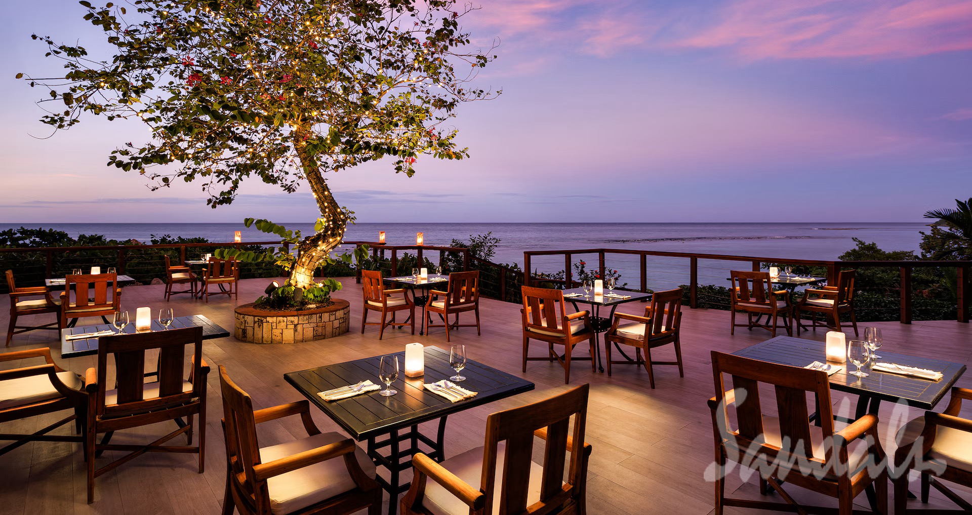 A candlelit oceanfront dinner deck at dusk at Sandals Jamaica Ocho Rios