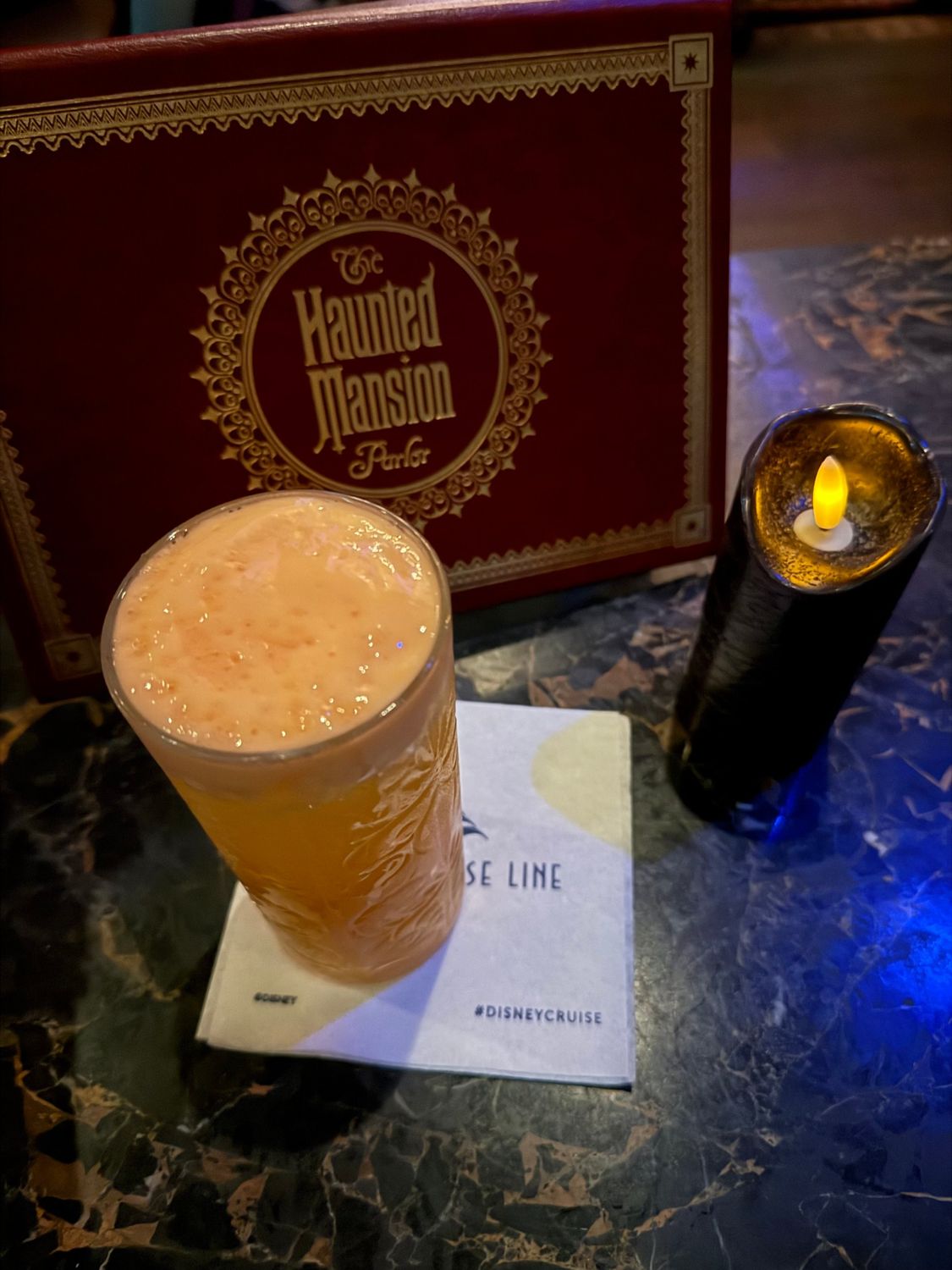 A frothy cocktail served on a paper napkin beside the menu at the Haunted Mansion Parlor